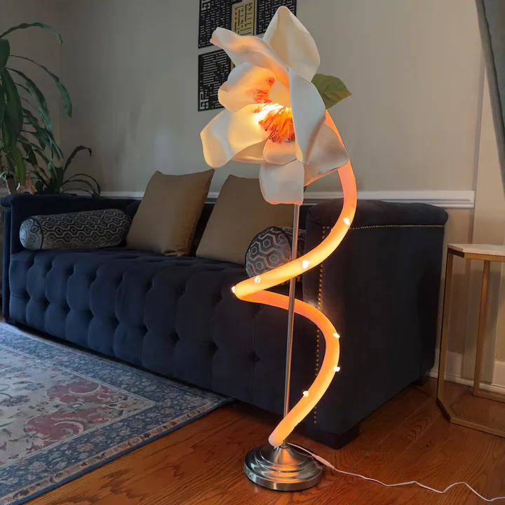 White magnolia sculptural floor lamp glowing beside a navy sofa