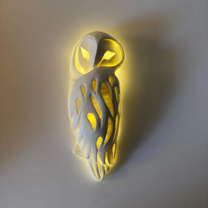 Pierced owl sculptural wall sconce with light glowing through its feathers